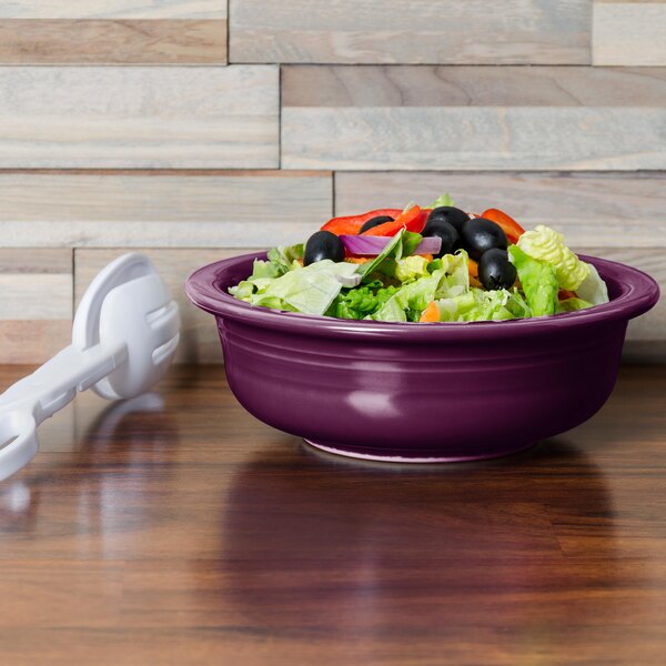 A close-up of a purple Fiesta serving bowl filled with salad and olives.