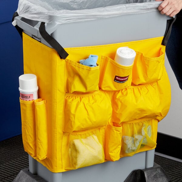 A person holding a yellow Rubbermaid Slim Jim trash can with a yellow vinyl bag.