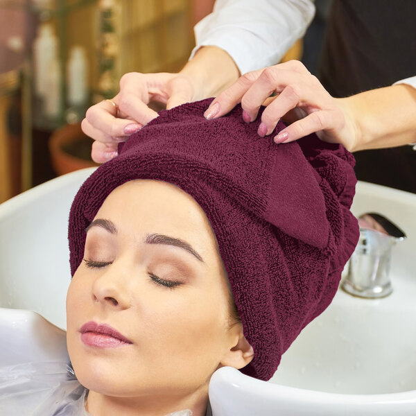 A woman with a Monarch Brands burgundy hand towel wrapped around her head getting her hair washed in a salon.
