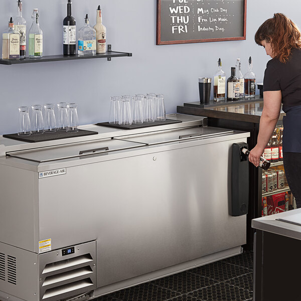 A woman standing at a stainless steel Beverage-Air deep well bottle cooler on a counter in a cocktail bar.