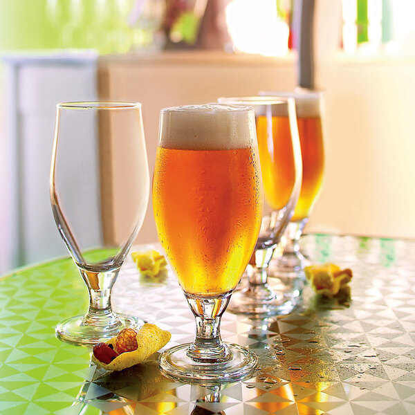 A group of Arcoroc Cervoise stemmed pilsner glasses filled with beer on a table.