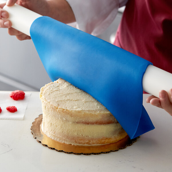 A person covering a cake with Satin Ice ChocoPan blue chocolate using a blue roll.