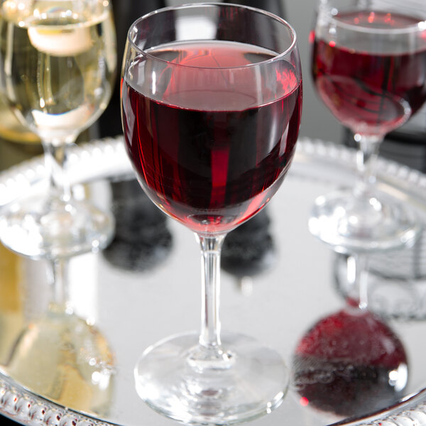 A Libbey chalice wine glass filled with red wine on a tray with other wine glasses.