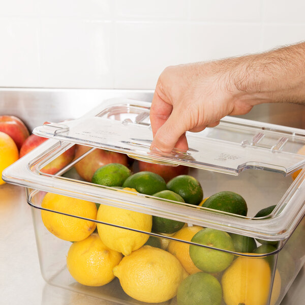 A hand using a Cambro clear plastic lid with a spoon notch to pick up a container of lemons.