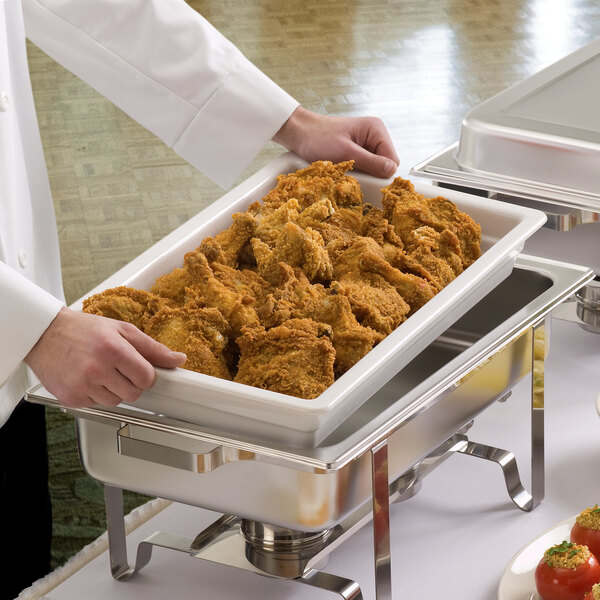 A person holding a tray of fried chicken in a Hall China food pan.