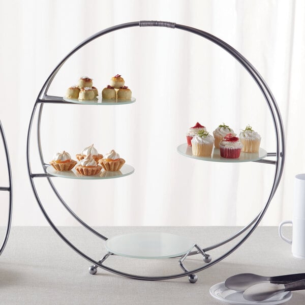 An American Metalcraft silver round stand with frosted glass plates holding cupcakes on a table.