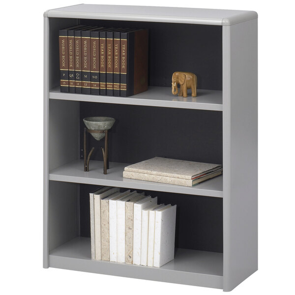 A grey Safco bookcase with books and a wooden elephant statue on the top shelf.