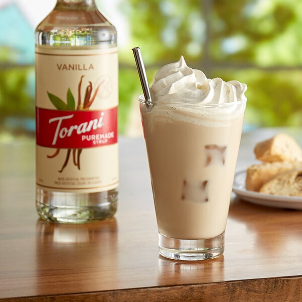 A glass of vanilla milkshake with a straw next to a bottle of Torani Puremade Vanilla Flavoring Syrup.