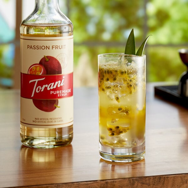 A glass of juice next to a bottle of Torani Puremade Passion Fruit flavoring syrup.