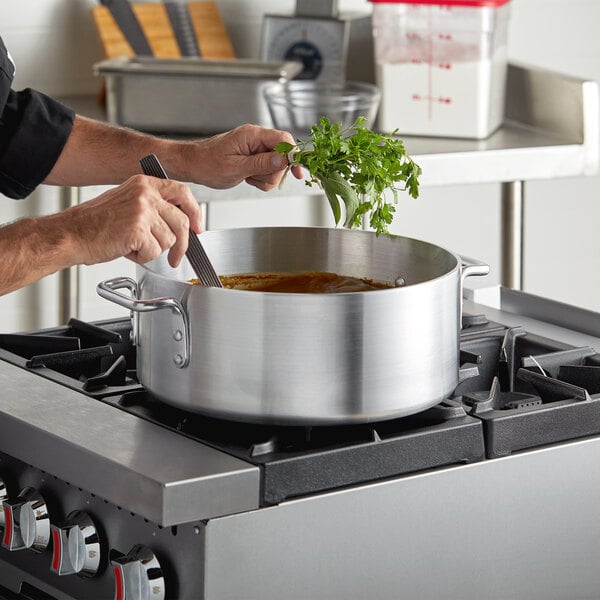 A chef cooking food in a Choice aluminum brazier on a stove.