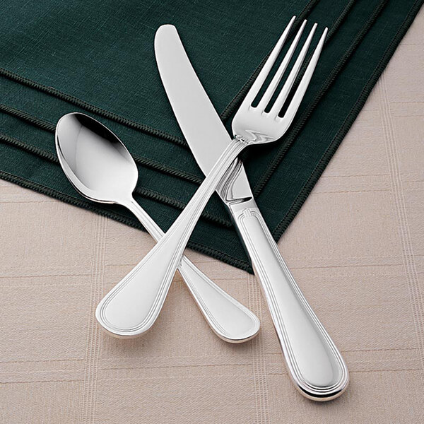 A Libbey stainless steel teaspoon and a knife on a green napkin.