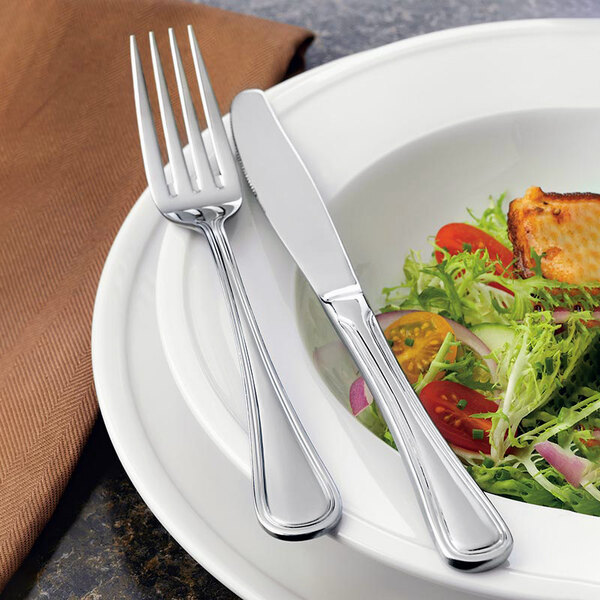 A plate of salad with a Libbey stainless steel dinner knife and fork.