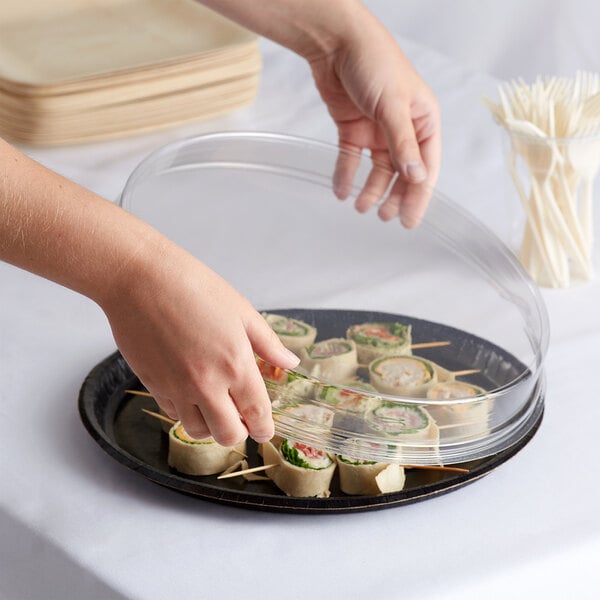 A person putting food on a clear round catering tray.