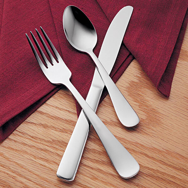 A Libbey Windsor Grandeur stainless steel teaspoon on a napkin with a fork and knife.