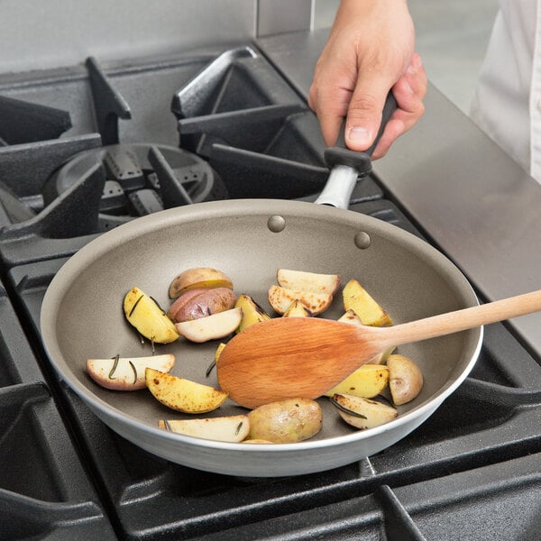 A person stirring potatoes and vegetables in a Vollrath non-stick fry pan on a stove.