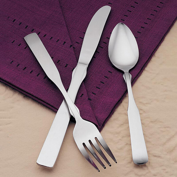 A Libbey stainless steel teaspoon with a fork and knife on a purple napkin.