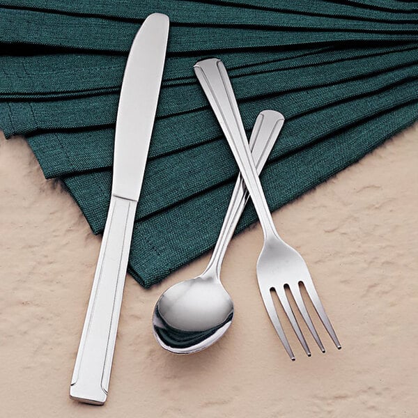 A Libbey stainless steel dinner fork on a napkin with a fork, knife, and spoon.