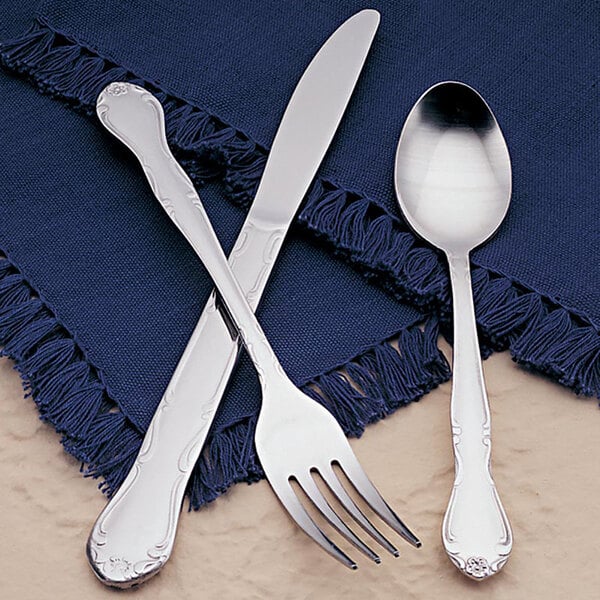 A close-up of a Libbey stainless steel teaspoon and fork on a blue cloth.