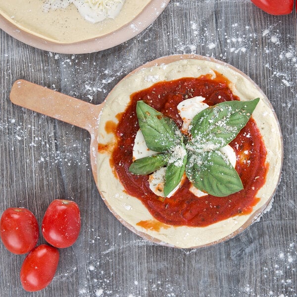 An American Metalcraft round pizza peel with a pizza in a pan with sauce and basil leaves on top.