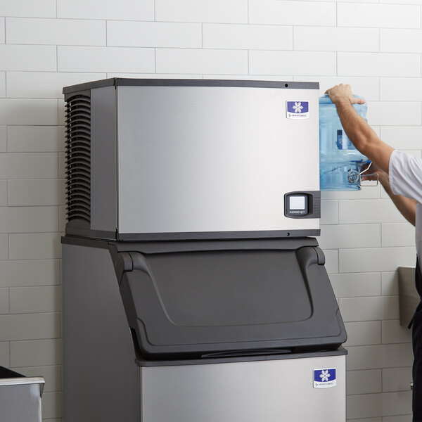 A man in a white shirt standing next to a large Manitowoc water cooled ice machine.