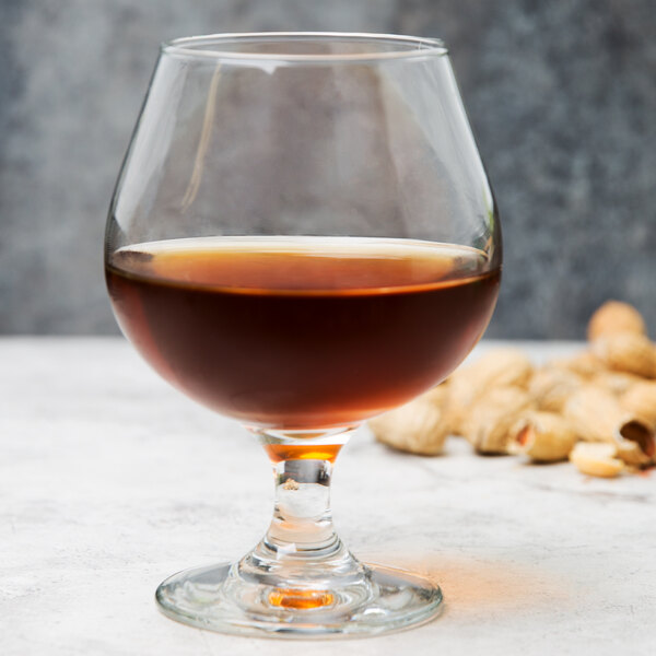 A Libbey brandy glass on a table filled with dark brown liquid.