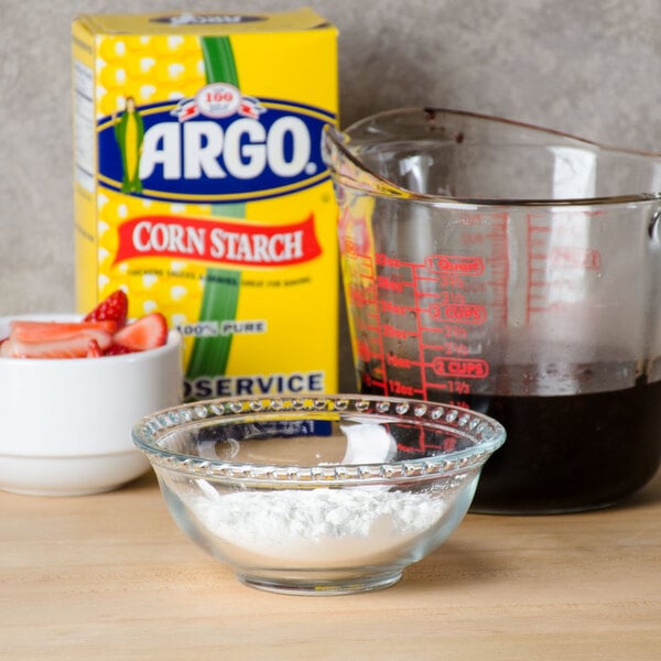 A glass bowl with Argo corn starch in it on a table with bowls of flour and strawberries.