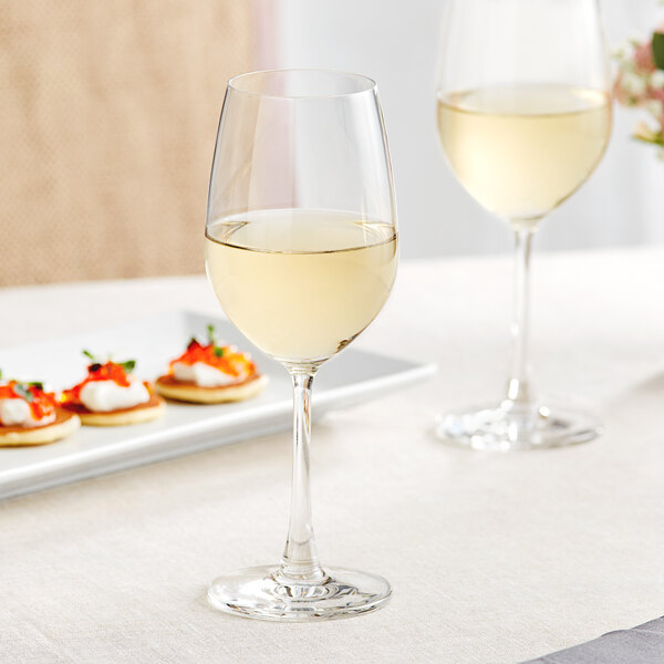Two Acopa Covella wine glasses filled with white wine on a table with food.