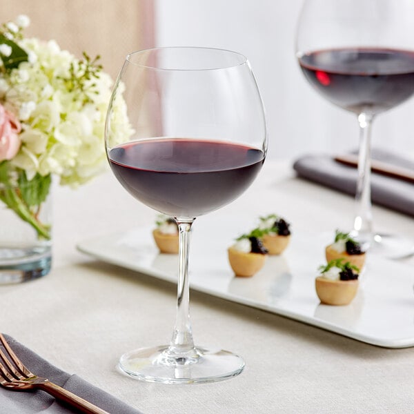 A table with a glass of red wine and food in wine glasses.