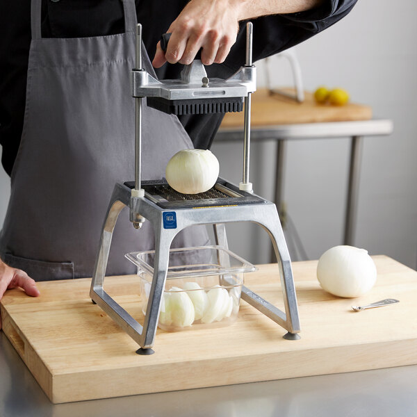 A man using a Vollrath vegetable slicer to cut onions on a cutting board.