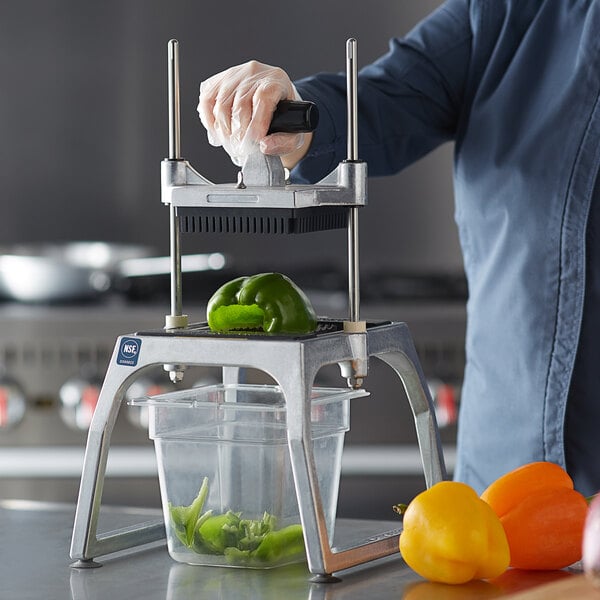 A person using a Vollrath vegetable cutter to slice a yellow bell pepper.