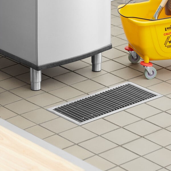 A floor with a Regency stainless steel floor water receptacle with a yellow bucket on wheels underneath.