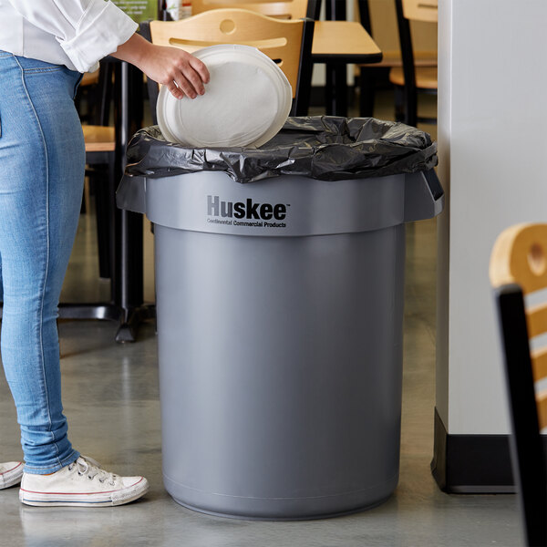 A person putting a white plate into a Continental grey trash can.