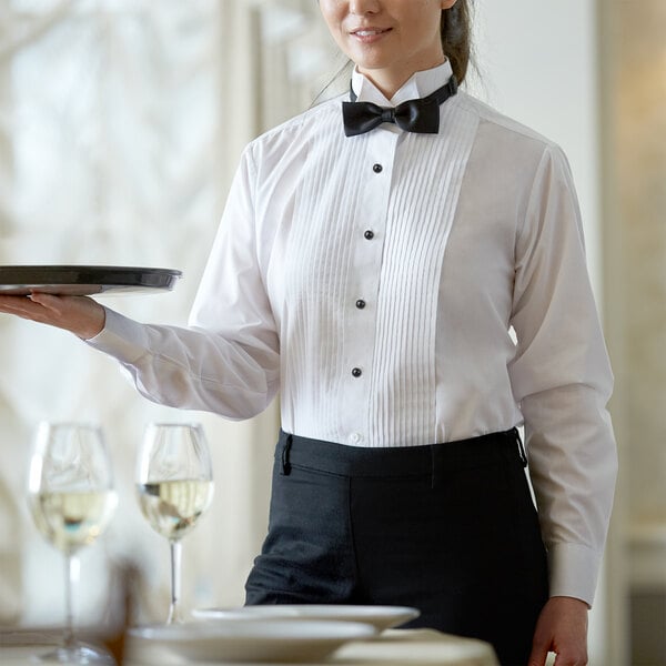 A woman in a white tuxedo shirt with a wing tip collar holding a tray with wine glasses.