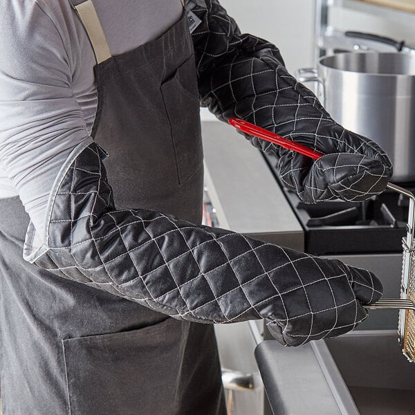 A person in a grey apron using a SafeMitt oven mitt to cook with a red utensil.