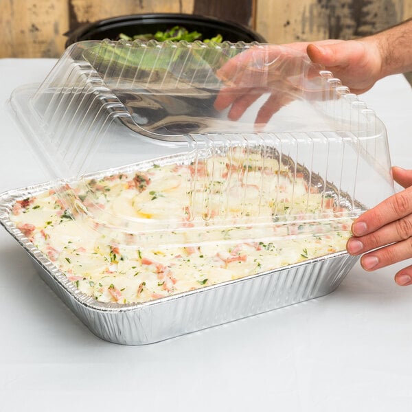 A person holding a Durable Packaging half size dome lid on a tray of food.