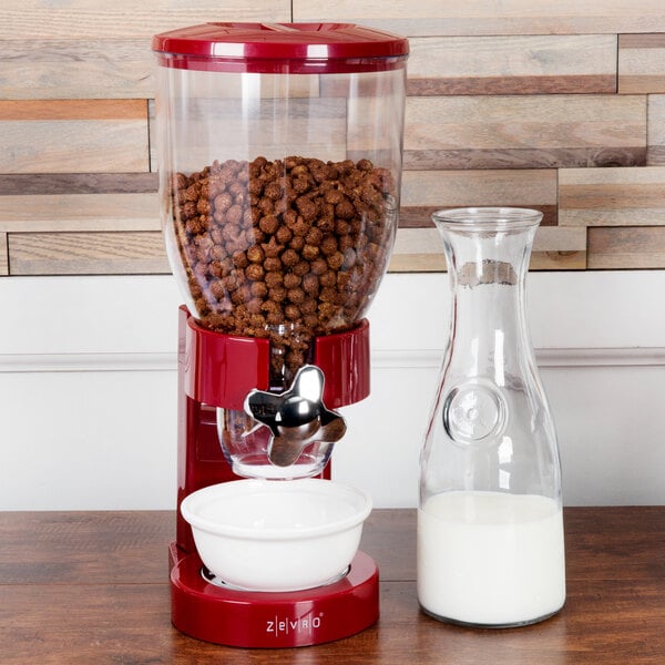 A Zevro red dry food dispenser with a white bowl of cereal on a red surface.