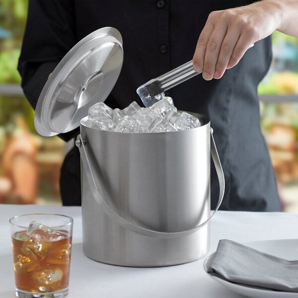 A woman using tongs to put ice in a Franmara stainless steel ice bucket.