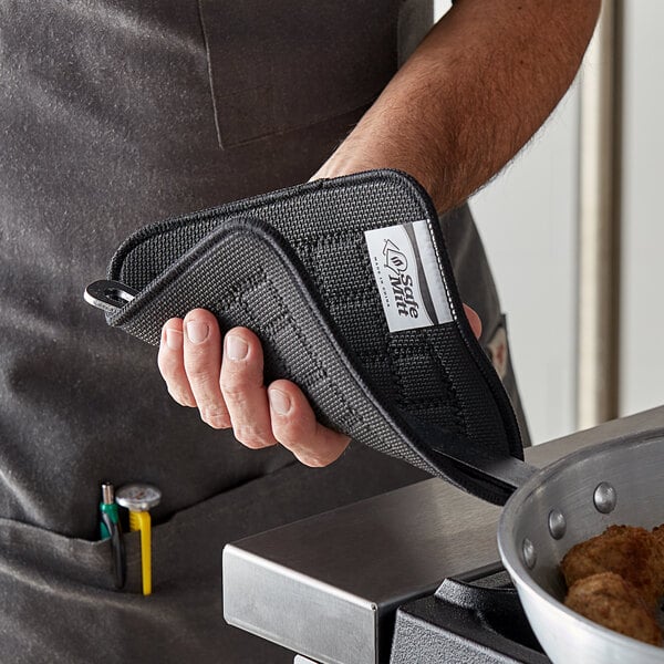 A person using a black SafeMitt to hold a pan of food.