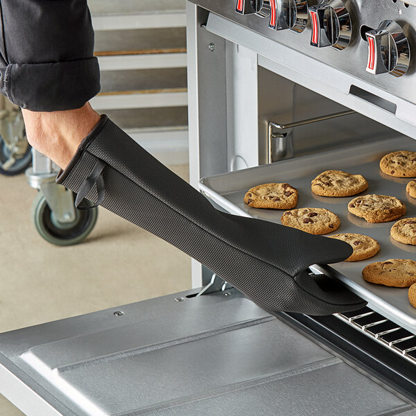 A person using a SafeMitt oven mitt to remove cookies from an oven.