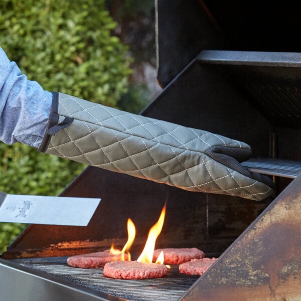 A person using a SafeMitt puppet style oven mitt to cook burgers on a grill.