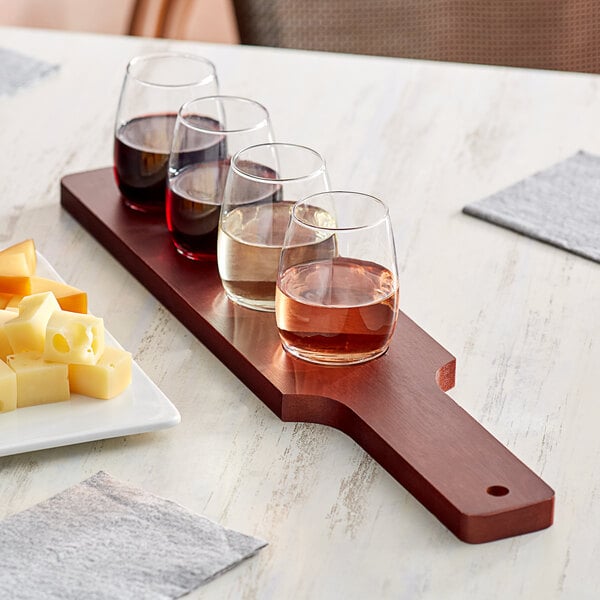 An Acopa mahogany flight paddle with stemless wine glasses of wine and cheese on a table.