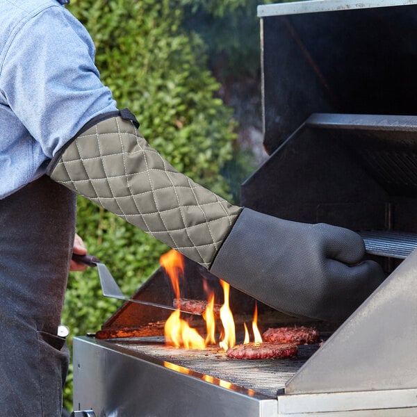 A man in a chef's outfit uses a SafeMitt to cook meat on a grill.