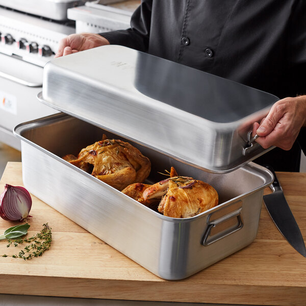 A person holding a Vollrath Wear-Ever aluminum double roaster pan with food inside.