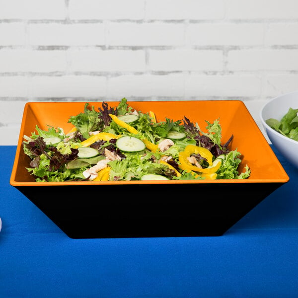 A bowl of salad with green leaves in a black Brasilia melamine bowl on a table.