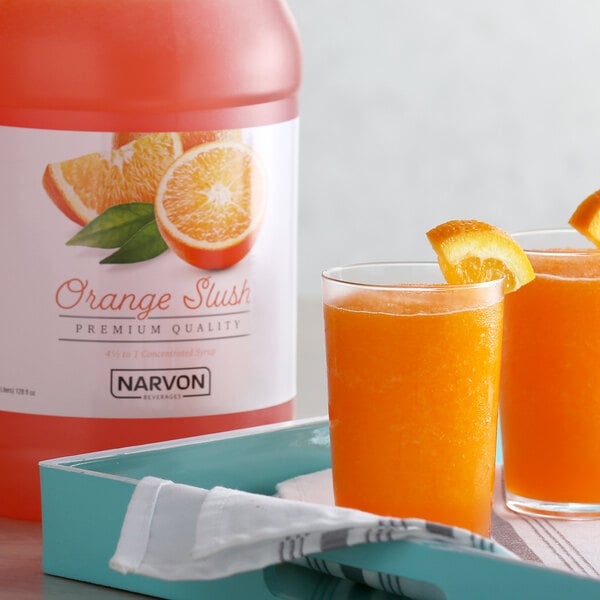 A glass of Narvon orange slushy with an orange slice on the rim on a table.