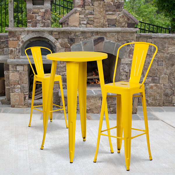 A Flash Furniture yellow metal bar table with two yellow stools on an outdoor patio.