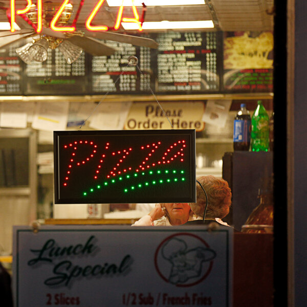 A rectangular LED pizza sign with red and green lights on a counter in a pizza parlor.