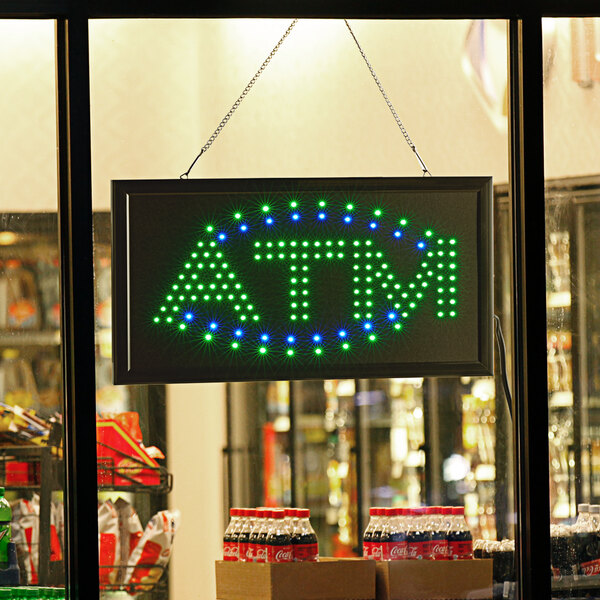 A rectangular blue and green LED ATM sign in a store window.