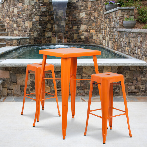An orange Flash Furniture bar height table with two orange square seat backless stools.