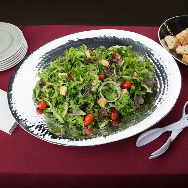 An American Metalcraft hammered stainless steel oval bowl filled with salad and a plate of bread.